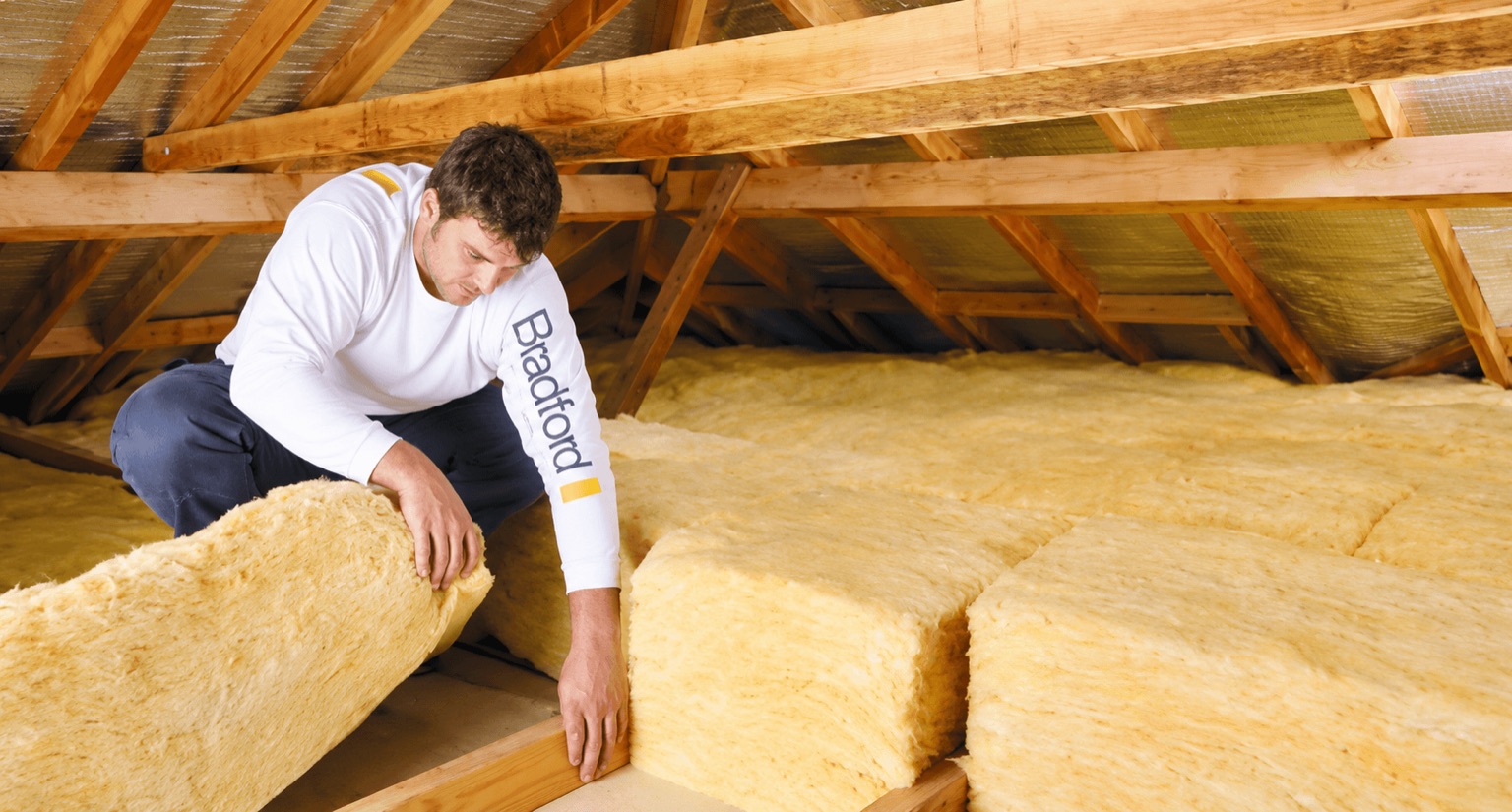 Installer laying Bradford insulation batts between ceiling joists in a roof space