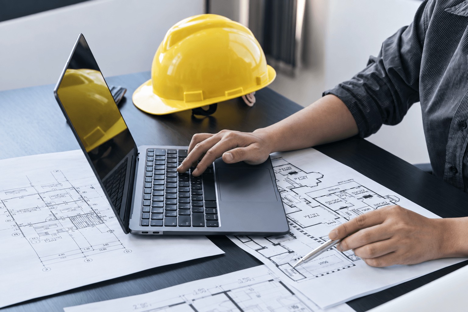 Consultant reviewing house plans on a laptop beside a yellow hard hat to recommend the right insulation