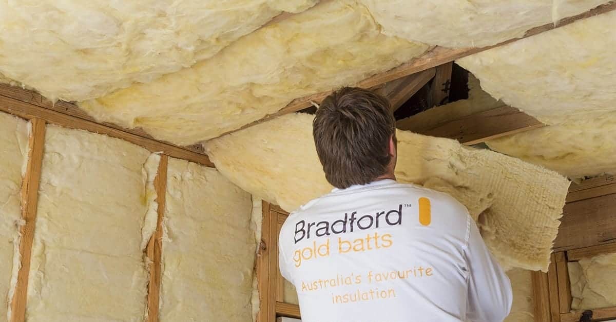 Installer fitting Bradford Gold insulation batts between ceiling and wall framing